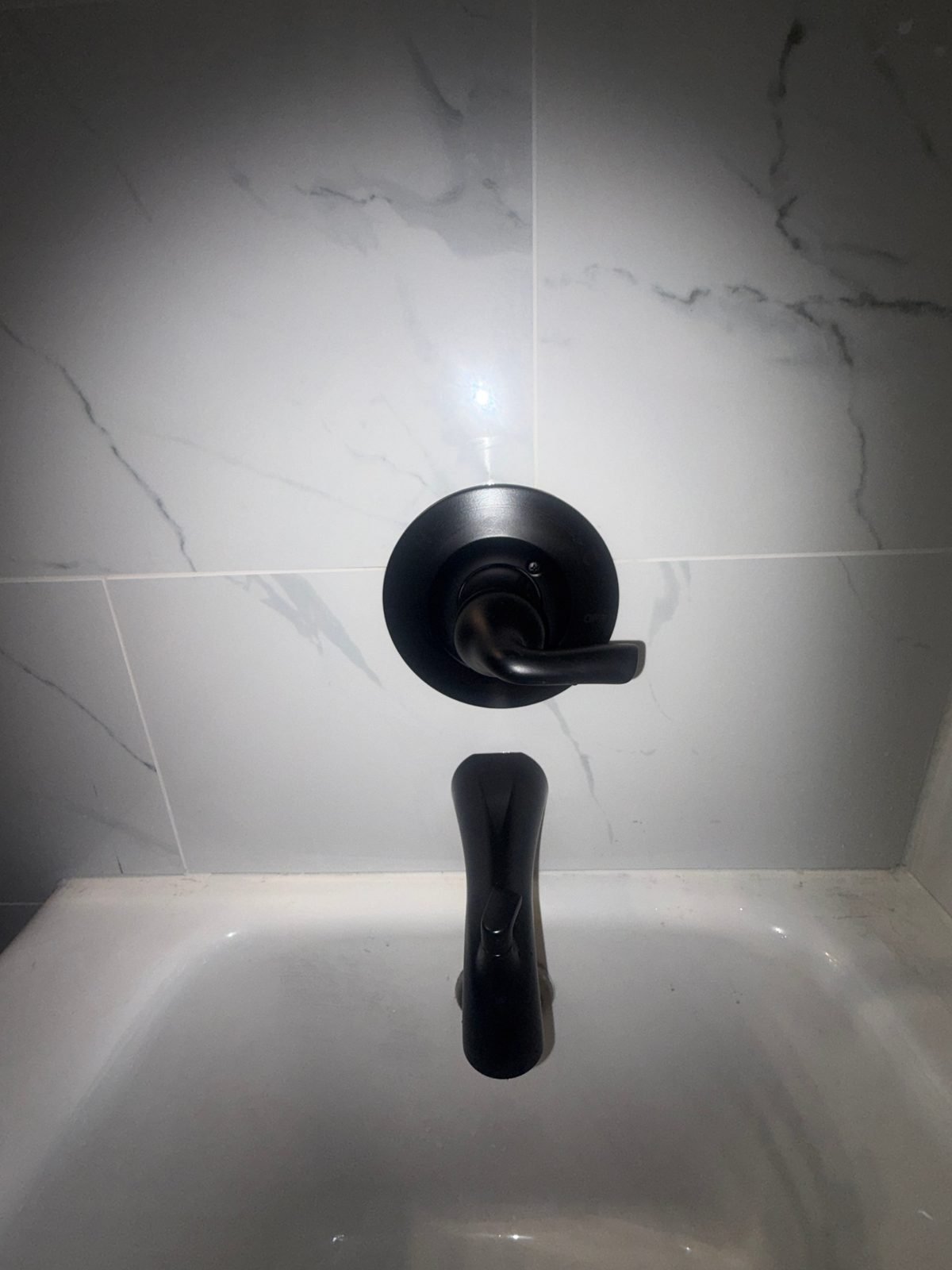 Close-up of the matte black Delta single-lever shower valve handle and tub spout with diverter above the tub in the remodeled Kennewick bathroom.