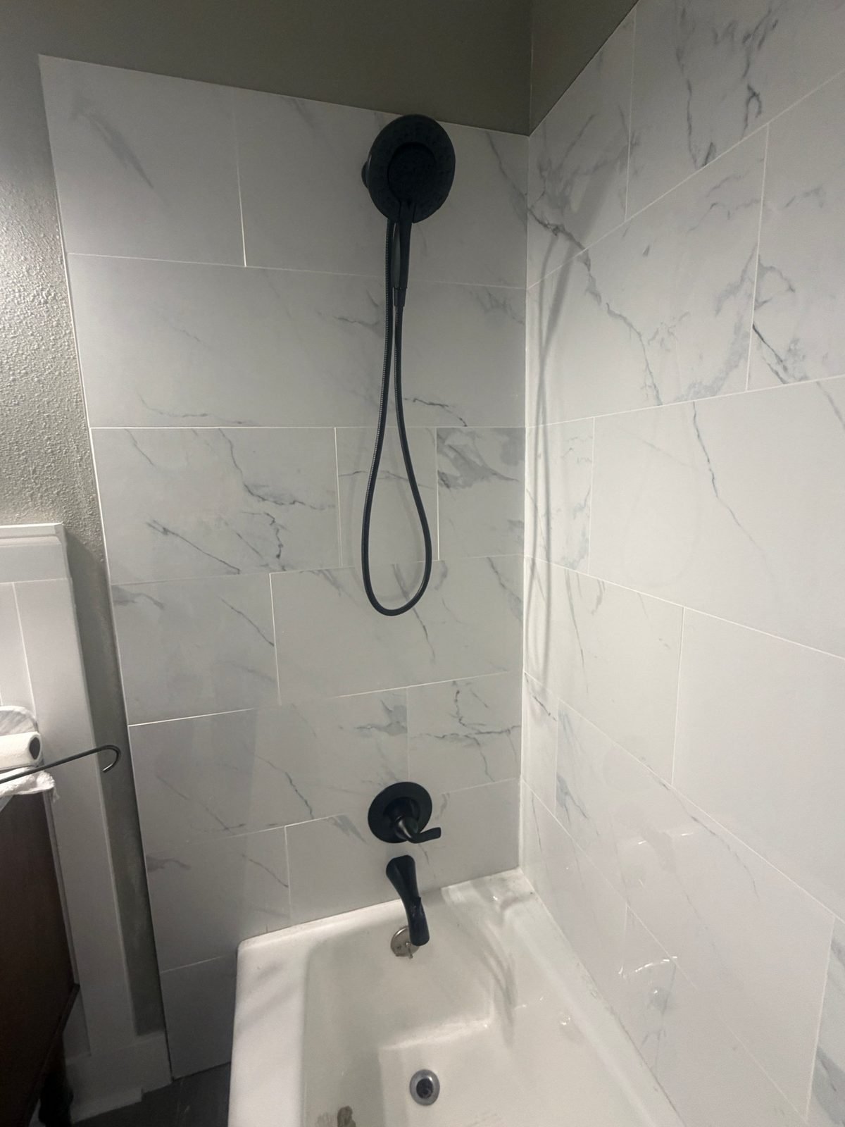 Finished tub and shower in a remodeled Kennewick bathroom with white marble-look tile, matte black Delta single-lever valve trim, a matching tub spout, and a two-in-one showerhead with a handheld sprayer.