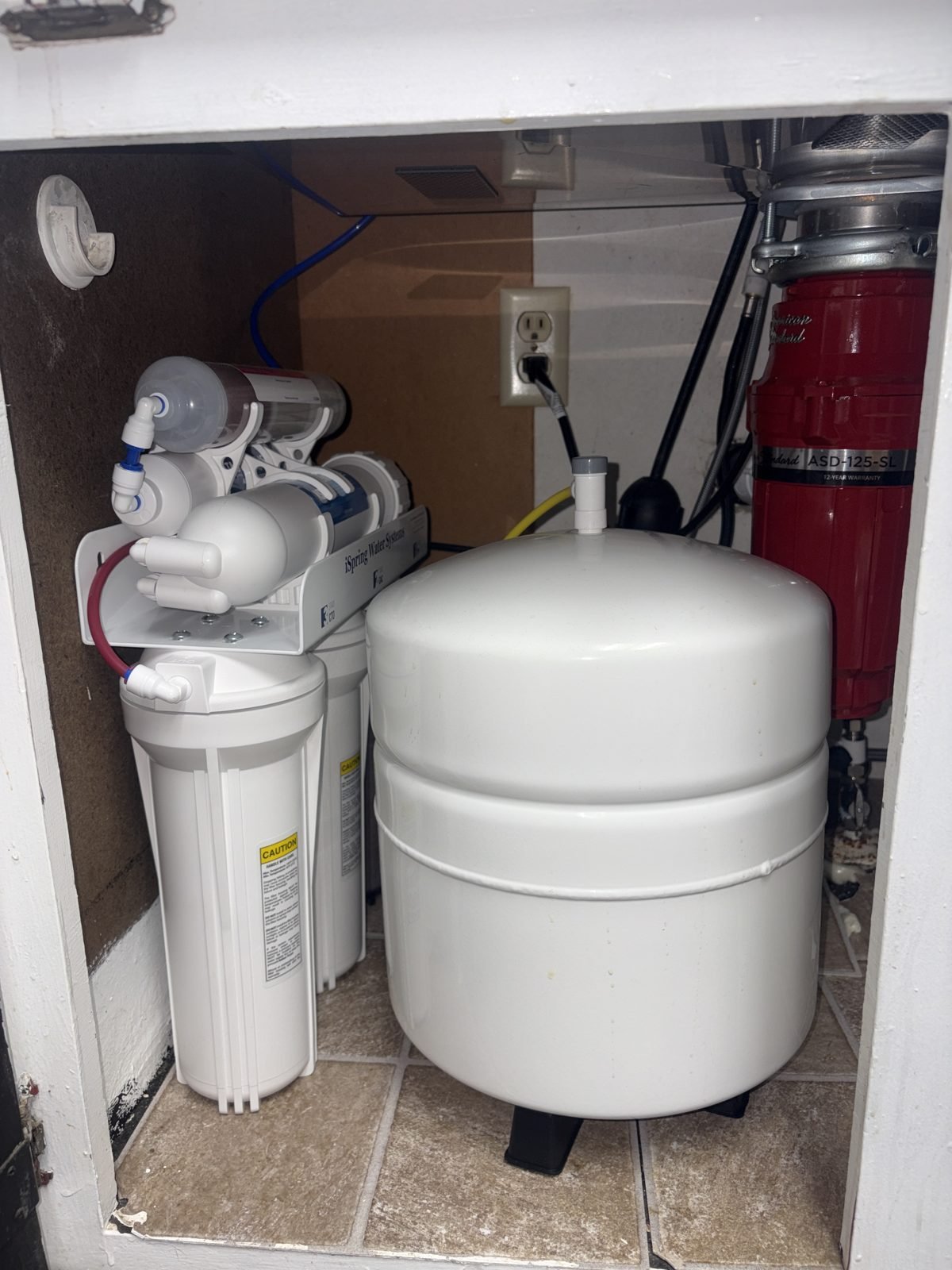 Under-sink reverse osmosis drinking water system installed in a Pasco home, showing the iSpring filter housings, membrane, and white storage tank mounted under the cabinet.