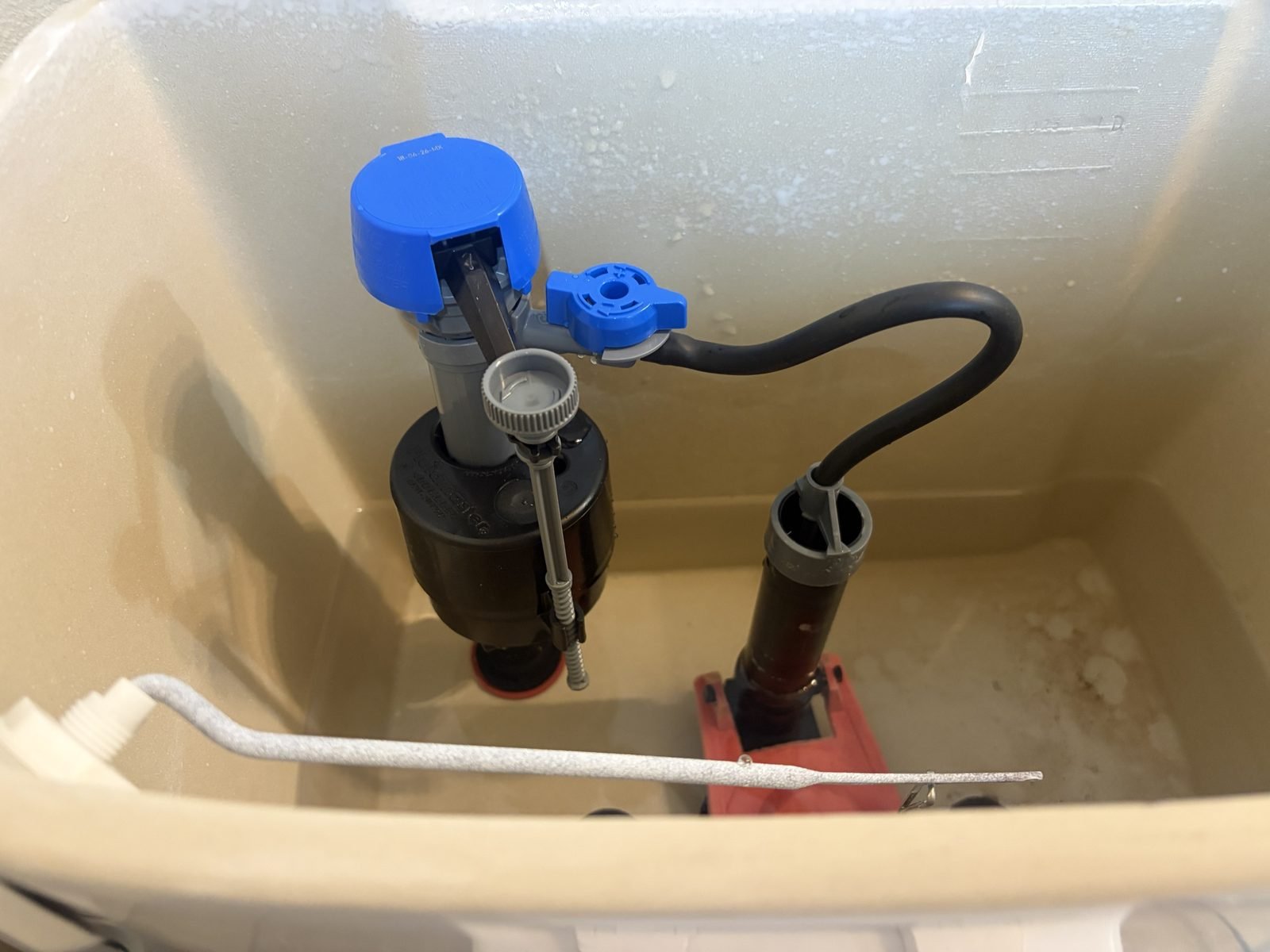 A newly installed toilet fill valve inside a toilet tank in Richland, with a blue cap, a fresh braided supply line connected at the shutoff, and the flush valve beside it.
