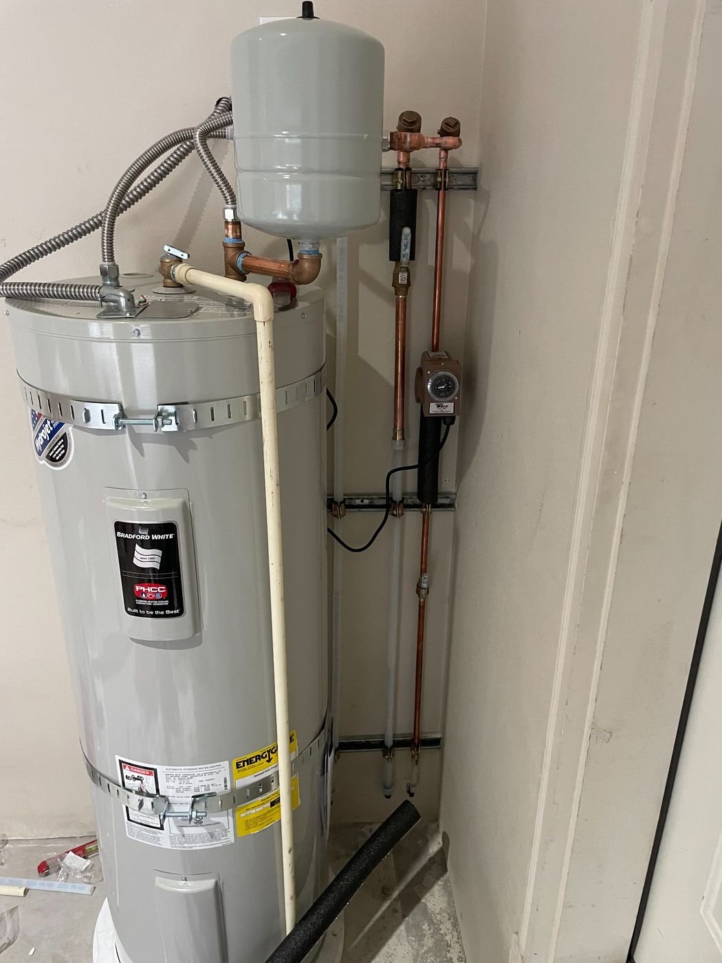 Newly installed Bradford White electric tank water heater in a Pasco home with a thermal expansion tank, seismic straps, copper supply lines with shutoff valves, and a relief-valve discharge line.